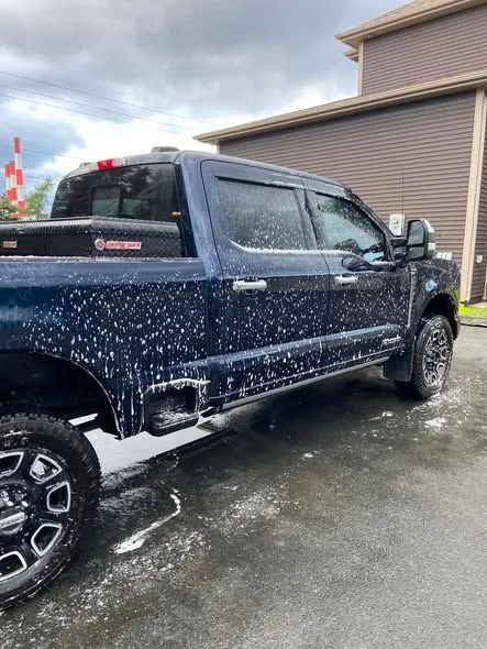 Dark blue pickup truck covered in wash suds in a driveway