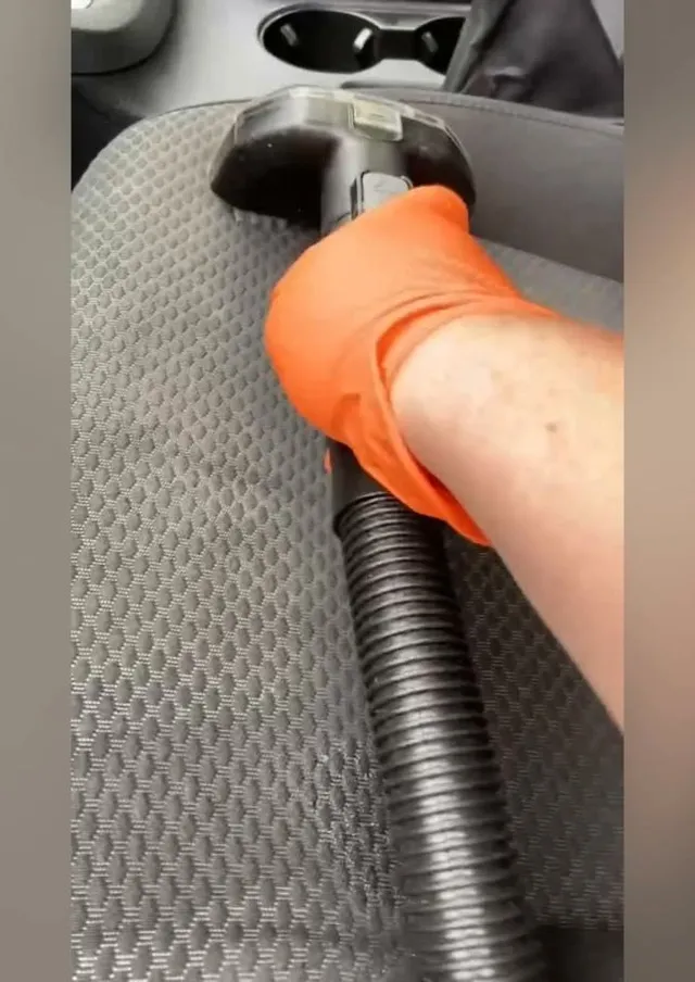 Gloved hand holding a vacuum hose over a car floor mat during an interior detail